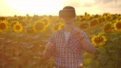The-young-player-is-working-in-VR-glasses.-He-is-engaged-in-the-working-process.-It-is-a-beautiful-sunny-day-in-the-sunflower-field.